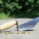 Giardiniere mentre rimuove erbacce tra le piastrelle con un utensile manuale.